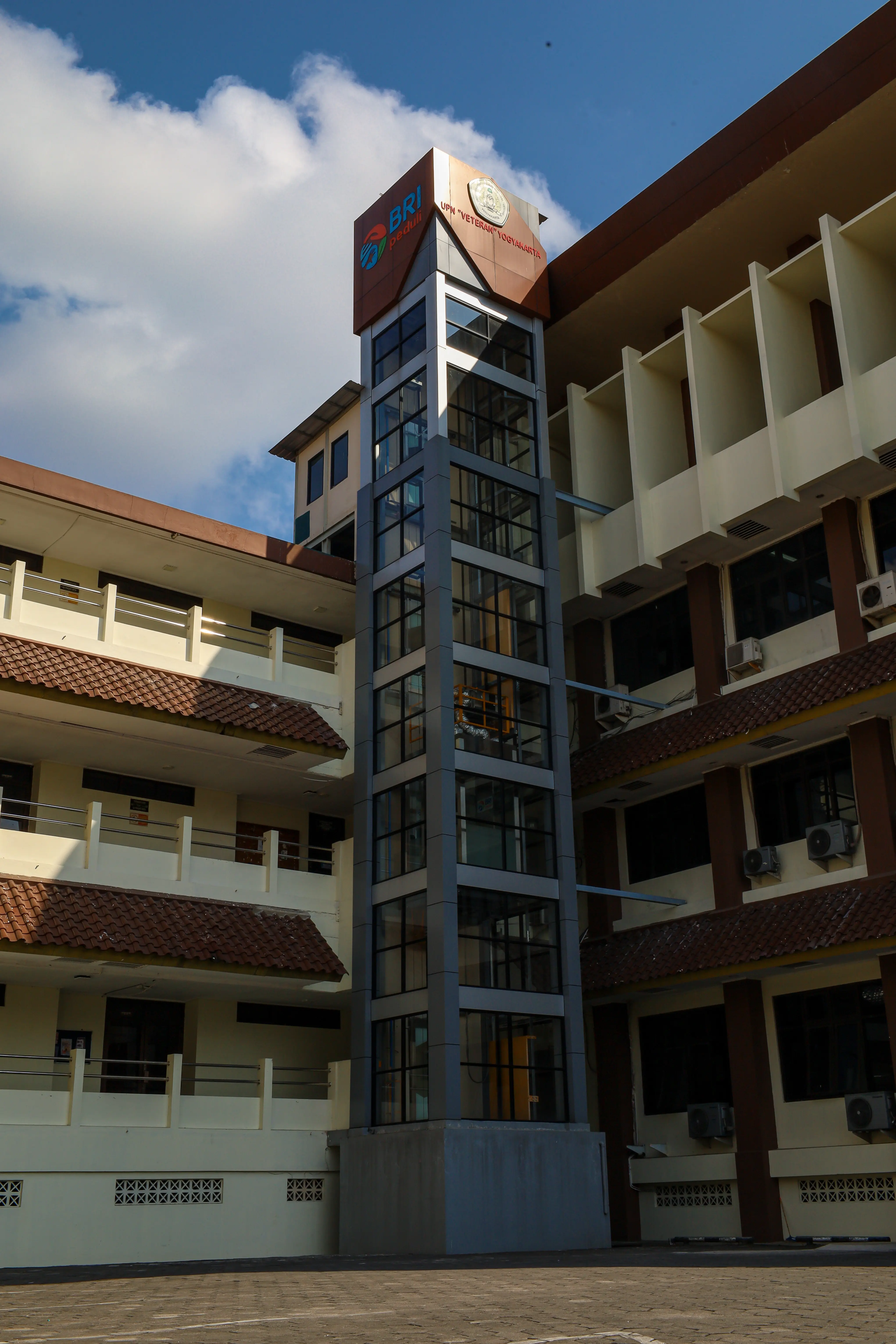 A glass elevator tower rising between the walkways of a school building